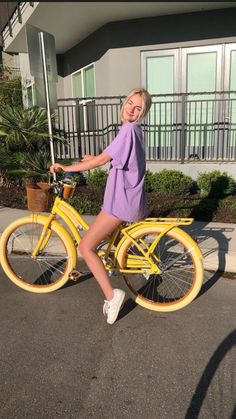 a woman in a purple dress is riding a yellow bike