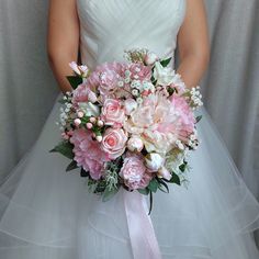 a bridal holding a bouquet of pink and white flowers on her wedding day in front of a gray backdrop