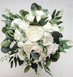 a bridal bouquet with white flowers and greenery on the stems in front of a white wall