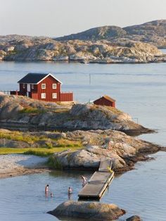 some people are standing in the water and there is a house on top of rocks