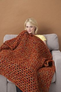 a woman is sitting on a couch wrapped in an orange and black flowered blanket