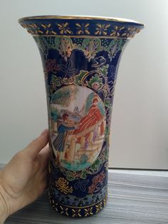 a hand holding a blue vase with paintings on it's sides and gold trimmings