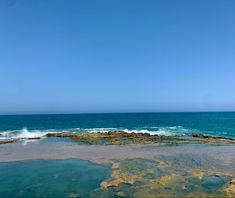 the ocean is blue and clear with waves coming in from the rocks on the shore