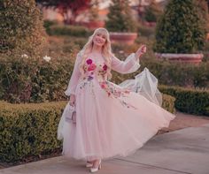 a woman in a pink dress is walking down the street with her arms out and smiling