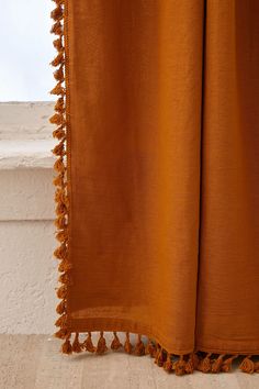 an orange curtain with tassels hanging from it's side on a ledge