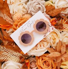 a pair of pink sunglasses sitting on top of some white and orange flowers next to a card