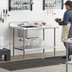 a woman standing in front of a kitchen sink holding a cup and looking at something on the wall