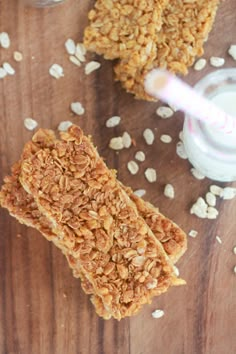 two granola bars sitting on top of a wooden table next to a glass of milk