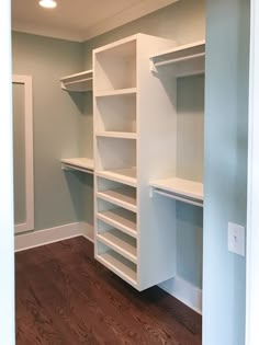 an empty walk in closet with white shelving and wood flooring on the side