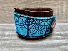 This item is authentically handmade of genuine leather, it has a hand printed image using indelible (permanent) ink. I've made this wrapping cuff out of soft leather, choose either scuffy brown or smooth black for the base. Machine stitched, it has an attached elastic that hooks over a button, so this cuff will adjust to fit most wrist sizes 5.75" to 7" in circumference. At the narrowest, the width of the cuff is 1.25" and at the widest it's 2".Only premium quality leather and supplies are used Handmade Turquoise Leather Bracelet Gift, Handmade Turquoise Leather Bracelet For Gift, Turquoise Leather Bracelet Gift, Unique Turquoise Leather Bracelet Gift, Handmade Blue Bracelets For Everyday, Hand Tooled Leather Bracelet For Gift, Hand-tooled Cuff Bracelets As Gift, Hand Tooled Cuff Bracelets As A Gift, Hand Tooled Cuff Bracelet For Gift