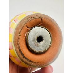 a hand holding an old ceramic vase with a hole in the center that has been painted yellow and red