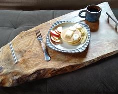 a wooden tray topped with sliced apples and pancakes next to a cup of coffee on top of a couch