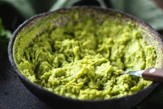 a bowl filled with guacamole on top of a table next to a knife