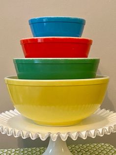 four colorful bowls are stacked on top of each other in a white cake stand with green and yellow patterned tablecloth