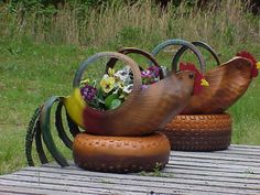 two wooden chickens sitting on top of tires with flowers in their heads and one chicken standing behind them