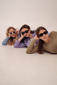 three women wearing sunglasses laying on the ground with their hands behind their heads and looking at the camera