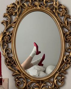 a woman's legs in red high heels are reflected in a gold framed mirror