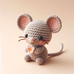 a small crocheted mouse sitting on top of a pink surface with one eye open