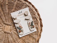 a pair of earrings sitting on top of a wicker basket next to a magazine