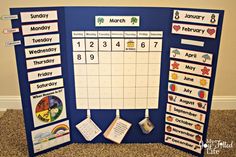 a blue bulletin board with calendars and magnets on it in front of a carpeted wall