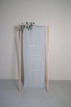 a menu hanging on a wooden frame in front of a white wall with green leaves