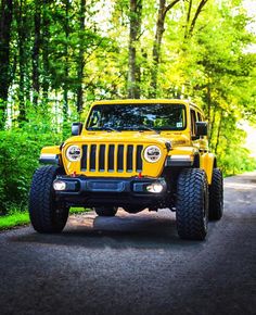 a yellow jeep is parked on the side of a road in front of some trees