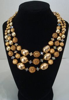 This is a beautiful three strand gold bead necklace by Lisner.  It is comprised of shiny gold beads, filigree gold beads, and textured gold beads. The large oval shiny gold beads are 19mm.  The filigree beads range from 14mm down to 9mm. Smaller textured and shiny beads complete the necklace.  In addition there are clear crystal AB pinched bicone beads and gold connector beads. The J-hook is signed Lisner. The wearable maximum length is 18 inches.  The necklace is in excellent vintage condition and would be perfect for the holidays.  Lots of sparkle. Sugar Beads, Glass Ball Ornaments, Gold Bead Necklace, Crystal Ab, Copper Pendants, Gold Texture, Gold Beads, Purple Gold, Bead Necklace