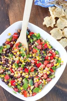 a white bowl filled with black beans, corn and tortilla chips next to a wooden spoon