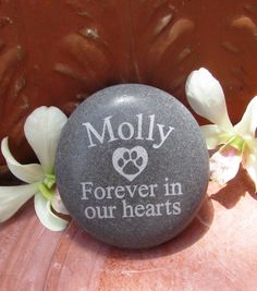 a rock that says moly forever in our hearts on it next to some flowers