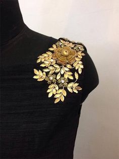 a black dress with gold flowers on the chest and collar, along with an embellished brooch