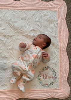 a baby laying on top of a white blanket next to a pink and white quilt