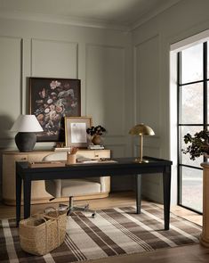 a room with a desk, lamp and pictures on the wall next to a large window