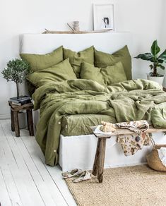 a bed with green sheets and pillows in a white room next to a potted plant