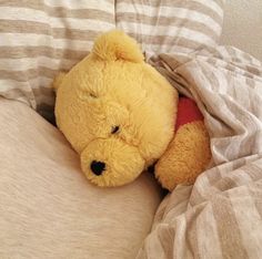 a yellow teddy bear laying on top of a bed covered in blankets and pillows with its eyes closed