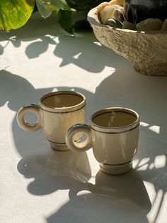 two coffee cups sitting on top of a table next to a bowl and planter