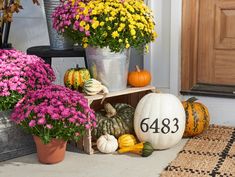 flowers and pumpkins are sitting on the front porch for fall time, with numbers painted on them