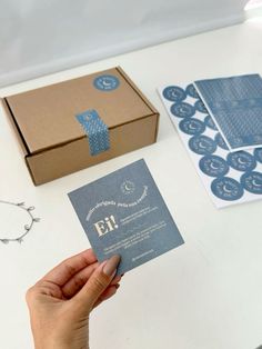 a person holding up a business card in front of a box and some other items