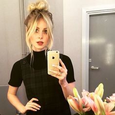 a woman taking a selfie in front of a mirror holding a cell phone and flowers