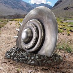 a large metal object sitting in the middle of a dirt field with mountains in the background