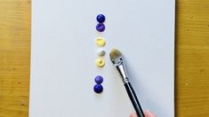 a hand holding a paintbrush over a piece of white paper with colored pebbles on it