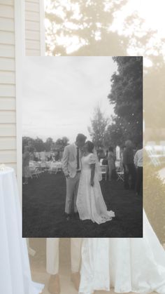 a couple standing next to each other in front of a building with people sitting on lawn chairs