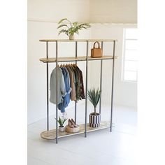 a rack with clothes and shoes on it in a room next to a potted plant