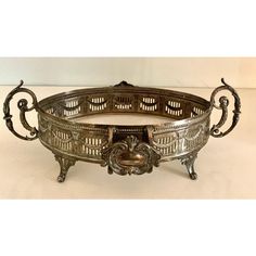 an ornate metal bowl with handles and carvings on the sides, sitting on a white surface