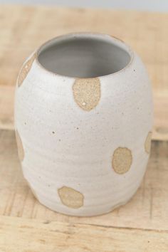 a white vase with gold polka dots on it sitting on a wooden table next to a planter