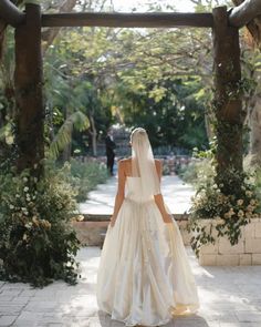 a woman in a wedding dress is walking through an archway with greenery on either side