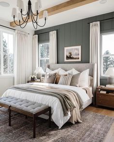 a bedroom with gray walls, white bedding and a chandelier hanging from the ceiling