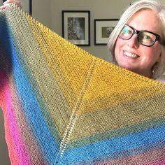 a woman holding up a multicolored knitted shawl