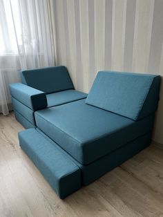 a blue couch sitting on top of a hard wood floor next to a white curtain