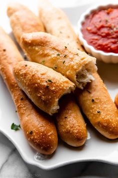 some breadsticks are sitting on a plate with sauce and ketchup in the background