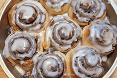 a pan filled with cinnamon rolls covered in icing on top of a wooden table